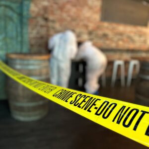 two blurred people in white crime suits, with a yellow crime scene do not enter tape in the foreground.