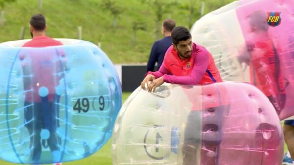Luiz suarez in his barcelona training kit standing in a bubble football with his teammates in the background facing away from him in their bubbles.