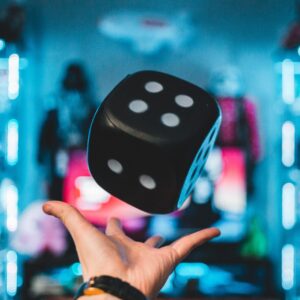 a hand throwing up a large black dice with white number spots. the background is blurred.