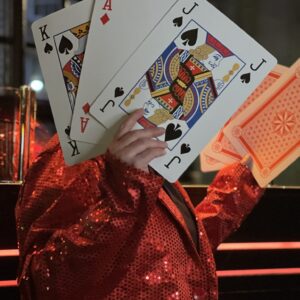 a person in a red sequin jacket, holding up six extra large playing cards, game show bonanza