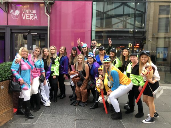 Hen party dressed in jockey outfits, posing with the hunky top gun host. The backdrop the gate complex newcastle.